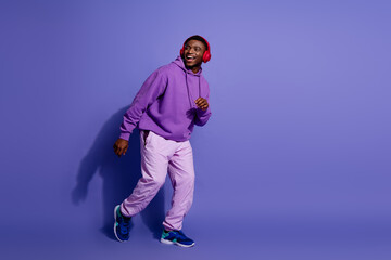 Young male enjoying music on headphones while wearing a purple hoodie and styled in casual trendy...