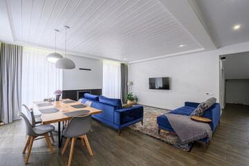 stylish living room featuring blue sofas, a wooden table with gray chairs, and a modern interior design with a white paneled ceiling