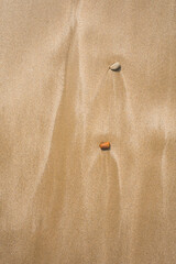 Two small stones resting on wet sand with delicate ripple patterns left by the receding tide at the beach in Essaouira, Morocco