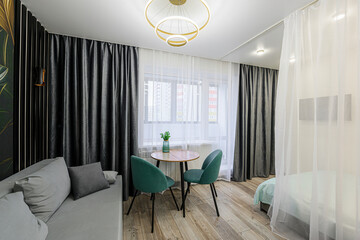 Cozy room with sofa, table, chairs, curtains, and a bright window. A modern chandelier hangs above