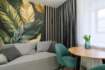 Cozy room with a sofa, round table, teal chair, and a wall featuring a tropical leaf design