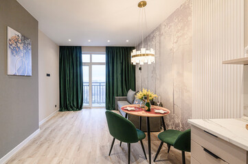 modern apartment with green accents: curtains, chairs, and floral art. A table is set for a celebration with champagne. A stylish chandelier hangs above