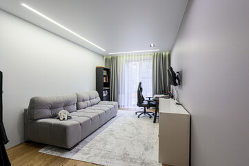 modern, brightly lit room features a gray couch, a desk with a gaming setup, and minimalist décor....