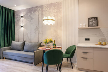 Cozy living area with a gray sofa, dining table set for two with green chairs, and a stylish...