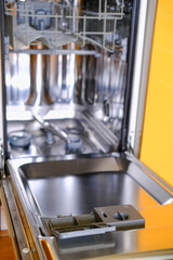 Open built-in dishwasher machine with empty space in modern yellow kitchen. Front view, vertical.