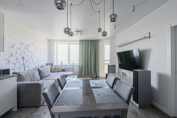 modern living room with gray sofa, dining table, TV, and unique chrome light fixtures. Dandelion...