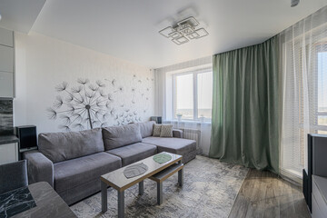 Modern living room with a gray sectional sofa, dandelion wall art, layered curtains, and nested coffee tables. Bright and airy ambiance