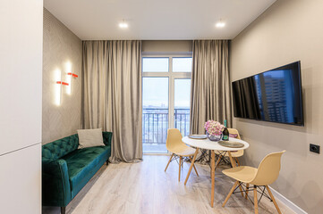 Cozy living room with a green sofa, dining area by the window, and a sleek TV. Modern and stylish apartment interior