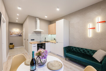 Cozy apartment interior: kitchen, dining area with flowers, and a green velvet sofa with modern...