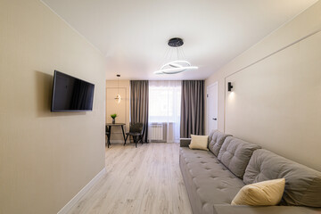 modern living room with a gray couch, a TV on the wall, a small dining table, and a contemporary chandelier