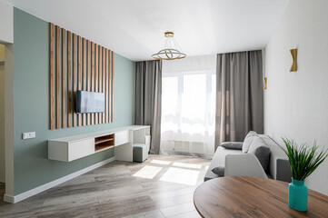 Bright living room with a TV on a wooden slat wall, a white floating cabinet, a grey sofa near a window with grey curtains, and a round wooden table