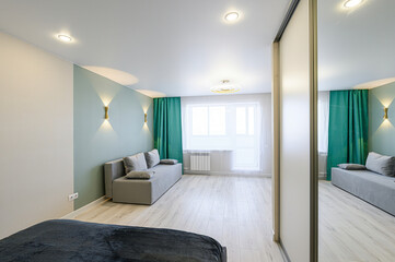 modern apartment featuring a gray sofa, green curtains, and mirrored closet doors, emphasizing...