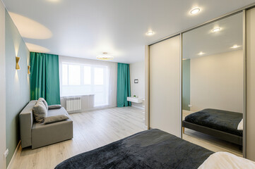 modern apartment featuring a gray sofa, green curtains, and mirrored closet doors, emphasizing clean lines and minimalist design