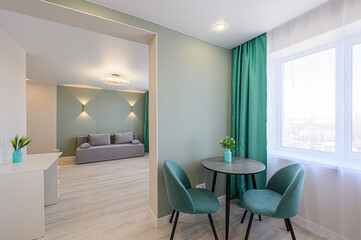 cozy room with a table, chairs, curtains, and a glimpse into another room with a sofa. The color palette is soothing