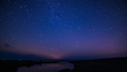 Fototapeta premium Star-filled night sky stretches above the calm reflective lake, featuring faint twilight glow upon the horizon, creating a serene and tranquil atmosphere under deep blue tones