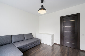 Clean room with a gray sofa, white dresser, and dark door. Black pendant lamp illuminates the space. Minimalist interior