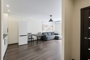 bright, modern living space featuring a gray sofa, dining set, white appliances, and wooden floors. The decor is minimalist with a large artwork and a pendant lamp