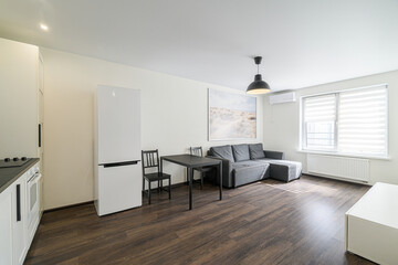bright room features a grey sofa, black table with chairs, a white refrigerator, and dark wood...