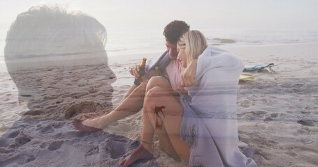 Couple wrapping blanket, sipping bottles on dusk beach with surfboard, senior overlay, copy space