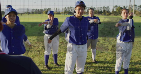 Stretching female baseball players pulling arms across chests on baseball field, wearing uniforms