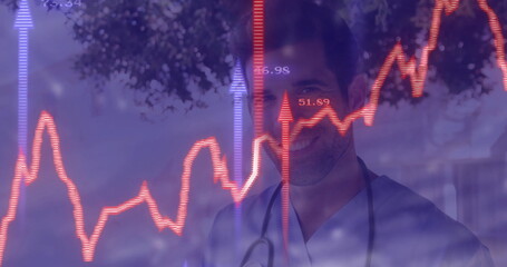 Standing male doctor wearing blue scrubs and stethoscope at hospital, with red-purple line graphs