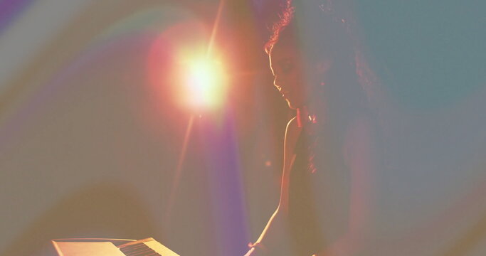 Performing woman musician playing electronic keyboard on dark stage, warm lens flare, copy space
