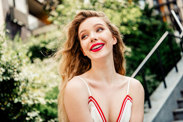 Cheerful young woman with vibrant red lips enjoying a sunny day outdoors in a casual setting with...