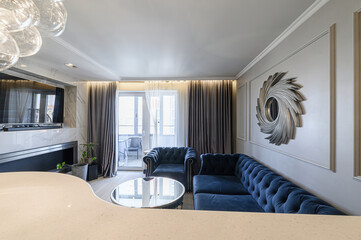 Elegant living room with blue velvet sofa, modern decor, fireplace, and balcony access. Stylish and...