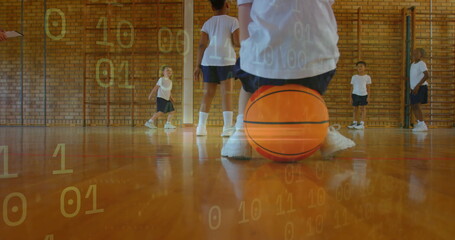 Kneeling child wearing white t-shirt navy shorts balancing on orange basketball in gym, wall bars