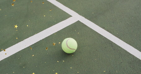 Resting tennis ball on outdoor tennis court near white lines, with gold star confetti, copy space