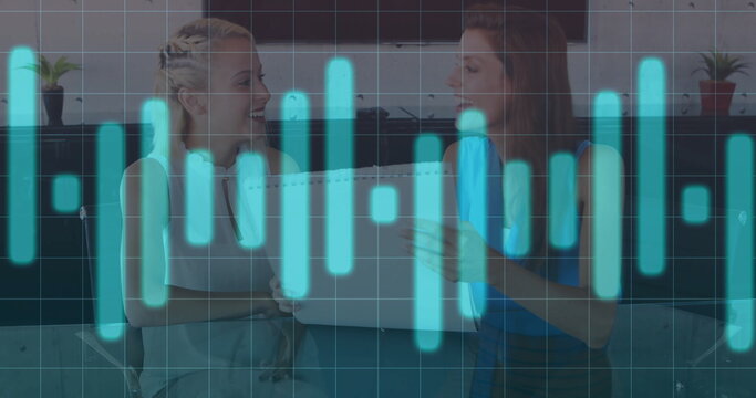 Collaborating two women reviewing spiral-bound report in conference room, with table and screens