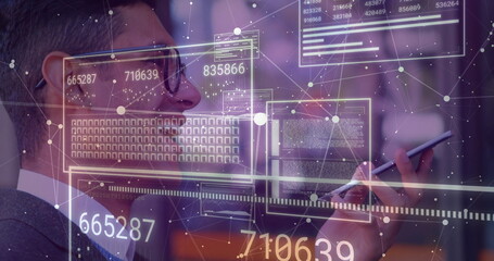 Scanning businessman in suit and glasses navigating holographic interface in office with smartphone