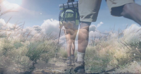 Trekking two hikers' lower bodies navigating narrow dirt path, with backpack and trekking pole