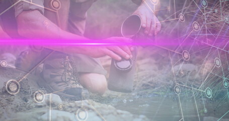 Filtering, hiker wearing boots pouring stream into filter unit at rocky creek, with network overlay