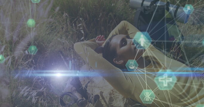 Lying female hiker resting on sloping meadow, with backpack, binoculars, lens tube, hex icons