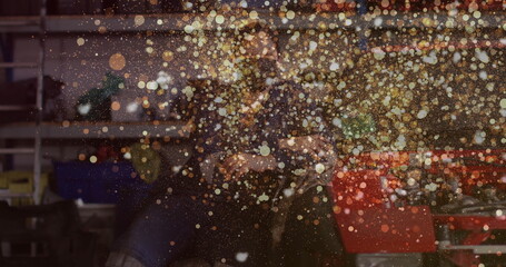 Grinding woman wearing dark jumpsuit spraying sparks onto metalwork in workshop, with angle grinder