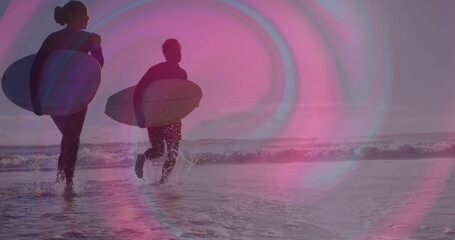 Walking duo of surfers carrying surfboards at sandy beach shoreline, with full-body wetsuits