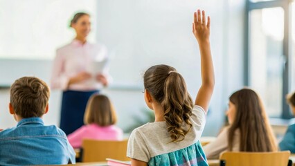A schoolgirl in the classroom raises her hand, preparing to answer a question. In the background, the teacher explains the material. The scene symbolizes active education.