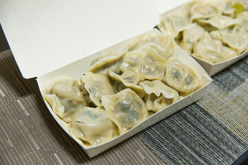 Box of freshly boiled dumplings with thin wrappers and juicy filling, arranged in a white takeout container on dining table
