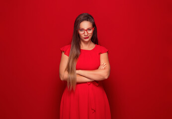 Young woman with smirking face expression looking at camera, isolated on red background. Frowned...