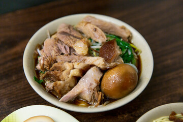 Taiwanese noodle soup with braised pork knuckle slices, soy sauce broth, leafy greens, bean sprouts, and braised egg served in a ceramic bowl