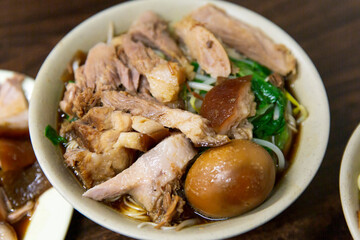 Taiwanese noodle soup topped with braised pork knuckle slices, soy sauce broth, leafy greens, bean sprouts, and marinated egg served hot in a bowl