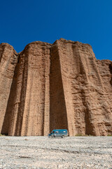 Travel van parked in front of massive red rock cliffs under a clear blue sky. Adventure road trip in a remote desert landscape, highlighting scale and freedom of exploration