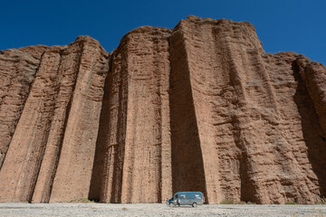 Travel van parked in front of massive red rock cliffs under a clear blue sky. Adventure road trip in a remote desert landscape, highlighting scale and freedom of exploration