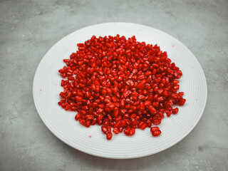 Fresh pomegranate seeds filling a white plate on a gray background