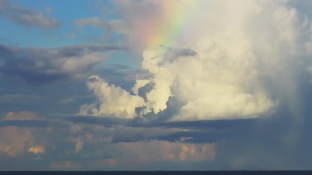 Aerial view of a rainbow forming within towering cumulus clouds above the Amazon rainforest in Tambopata, Peru, with dramatic light and shadow contrasting over the jungle horizon after rainfall