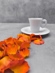 Orange rose petals leading to a white coffee cup on a gray table