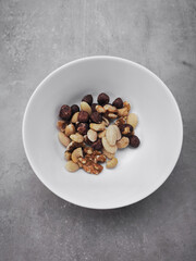 Mixed nuts filling a small white bowl on a gray surface