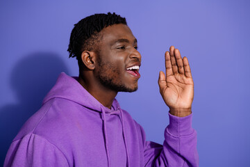 Portrait of a young stylish man in a purple hoodie making a cheerful gesture against a vibrant blue background