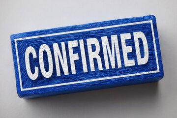 A blue block with the word confirmed in white letters sitting on a gray surface with a white border